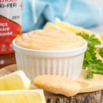 A small white dish and spoon with spicy mayo.