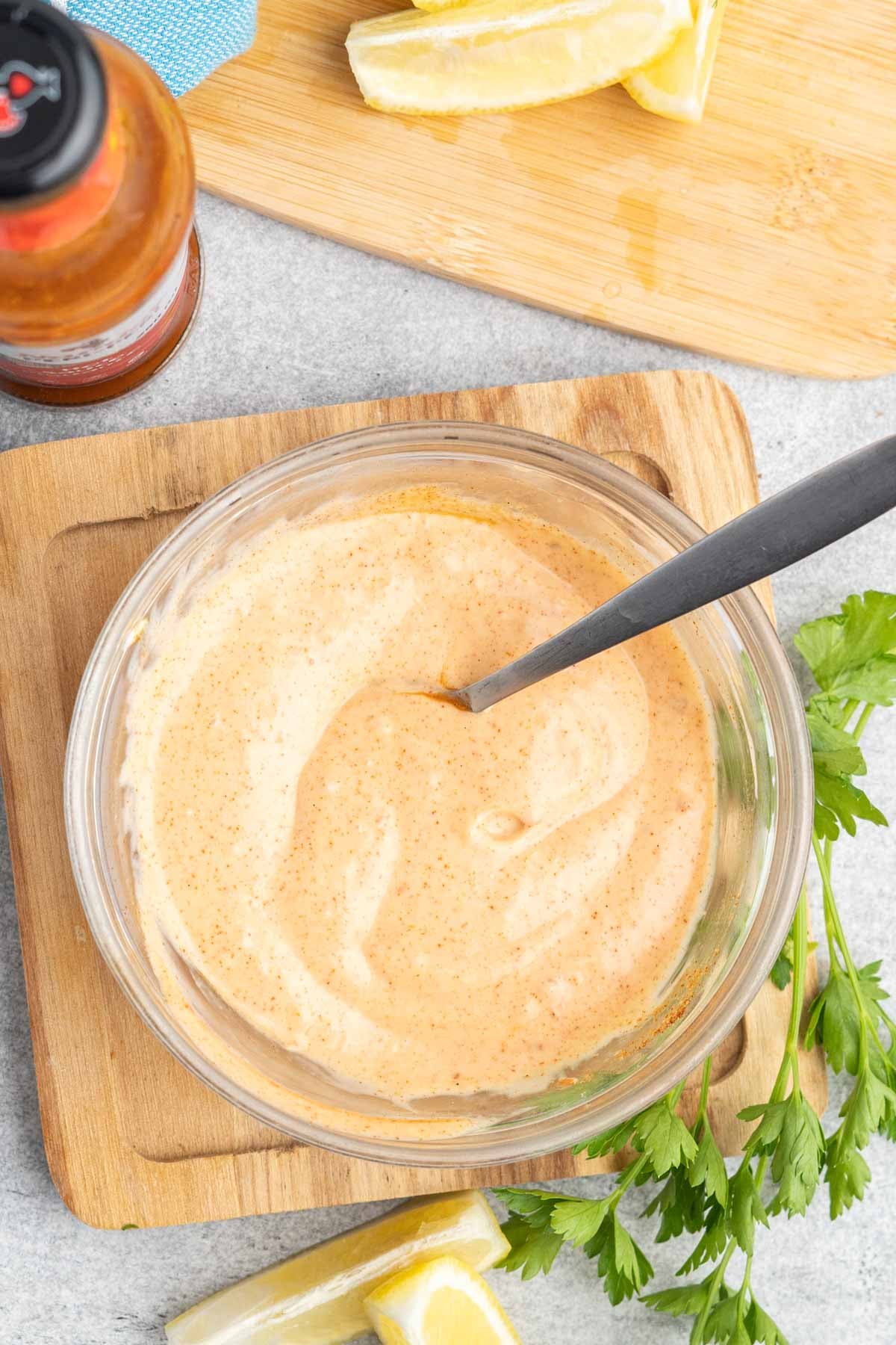 A glass bowl with mixed spicy mayo, lemon wedges and a bottle of peri-peri beside it. 