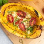 Spaghetti squash half filled with melted cheese and cherry tomatoes.