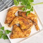 Four cooked chicken leg quarters on a platter.