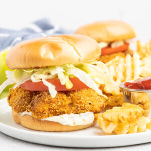 A crispy chicken burger with lettuce and tomato on a plate with fries.