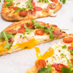 Naan bread pizza with egg, tomatoes, and arugula.