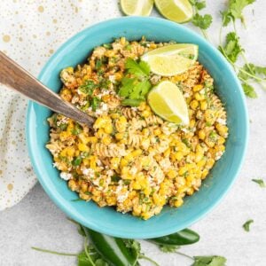 Corn pasta salad in a blue serving bowl with a wooden spoon.