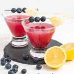 Blueberry martinis in stemless glasses garnished with fresh berries and lemon wedge.