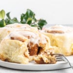 Three large cinnamon rolls on a plate, one with a bite removed.