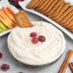 Eggnog dip in a bowl garnished with sugared cranberries and served with apples and cookies.