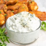 Blue cheese dip in a bowl with crumbled blue cheese and hot wings on a plate.
