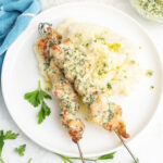 Parmesan garlic chicken skewers with a plate of mashed potatoes.