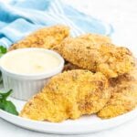 Breaded chicken strips on a plate with mustard dip.