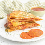 Tortillas filled with pizza sauce and pepperoni and a dish of pizza sauce on the side.