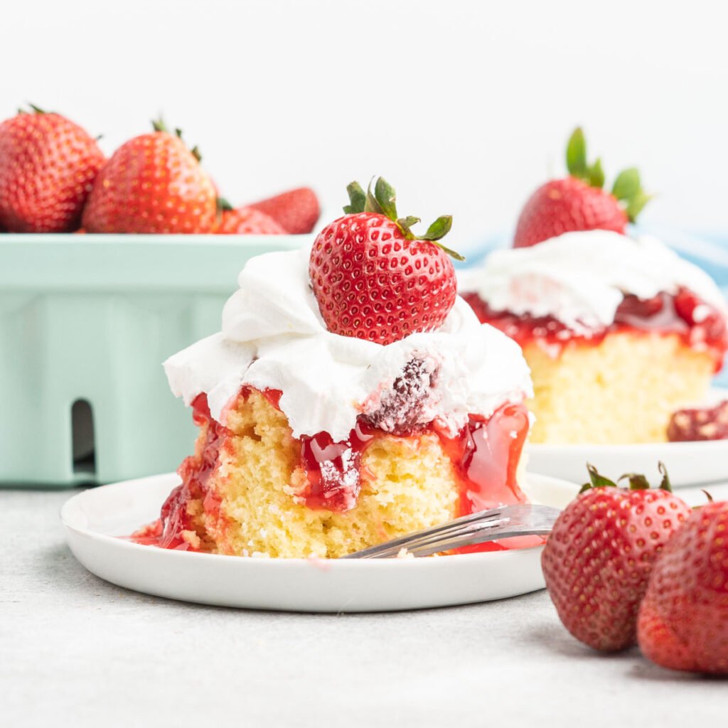 A slice of yellow cake with strawberry sauce and whipped topping.