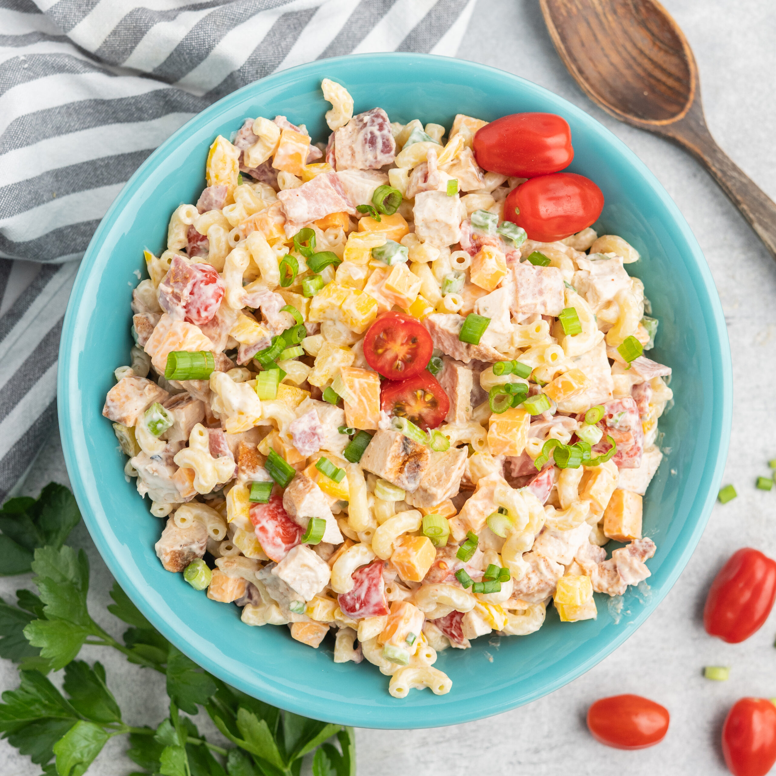 Pasta salad with chicken, bacon, cherry tomatoes, and green onion in a blue serving bowl.