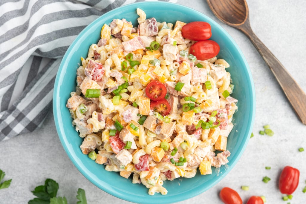 Pasta salad with chicken, bacon, cheese, and veggies in a blue serving bowl.