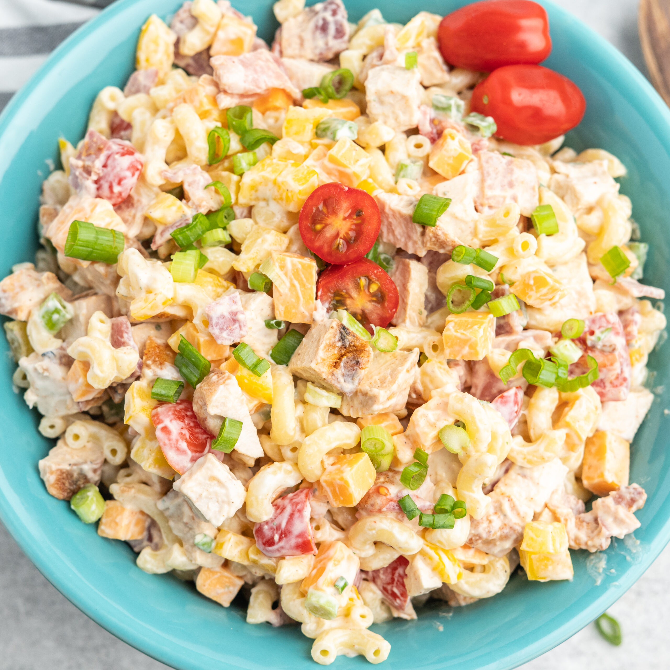 Pasta salad with chicken, bacon, cherry tomatoes, and green onion in a blue serving bowl.