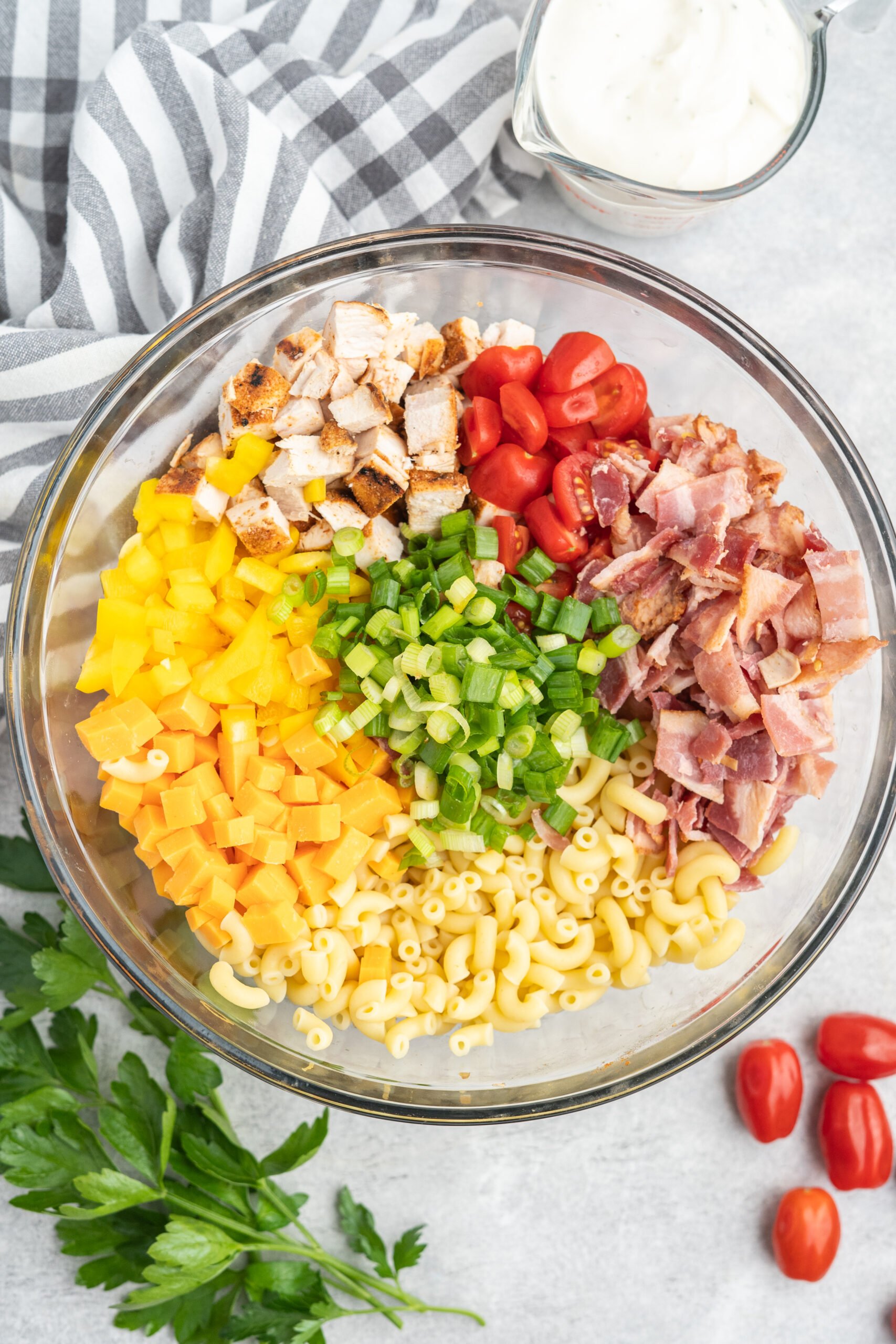 Cooked macaroni, diced bell peppers, bacon, chicken, cherry tomatoes, and green onions in a mixing bowl. 