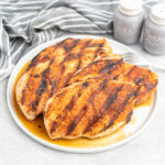 Four seasoned grilled chicken breasts on a plate.