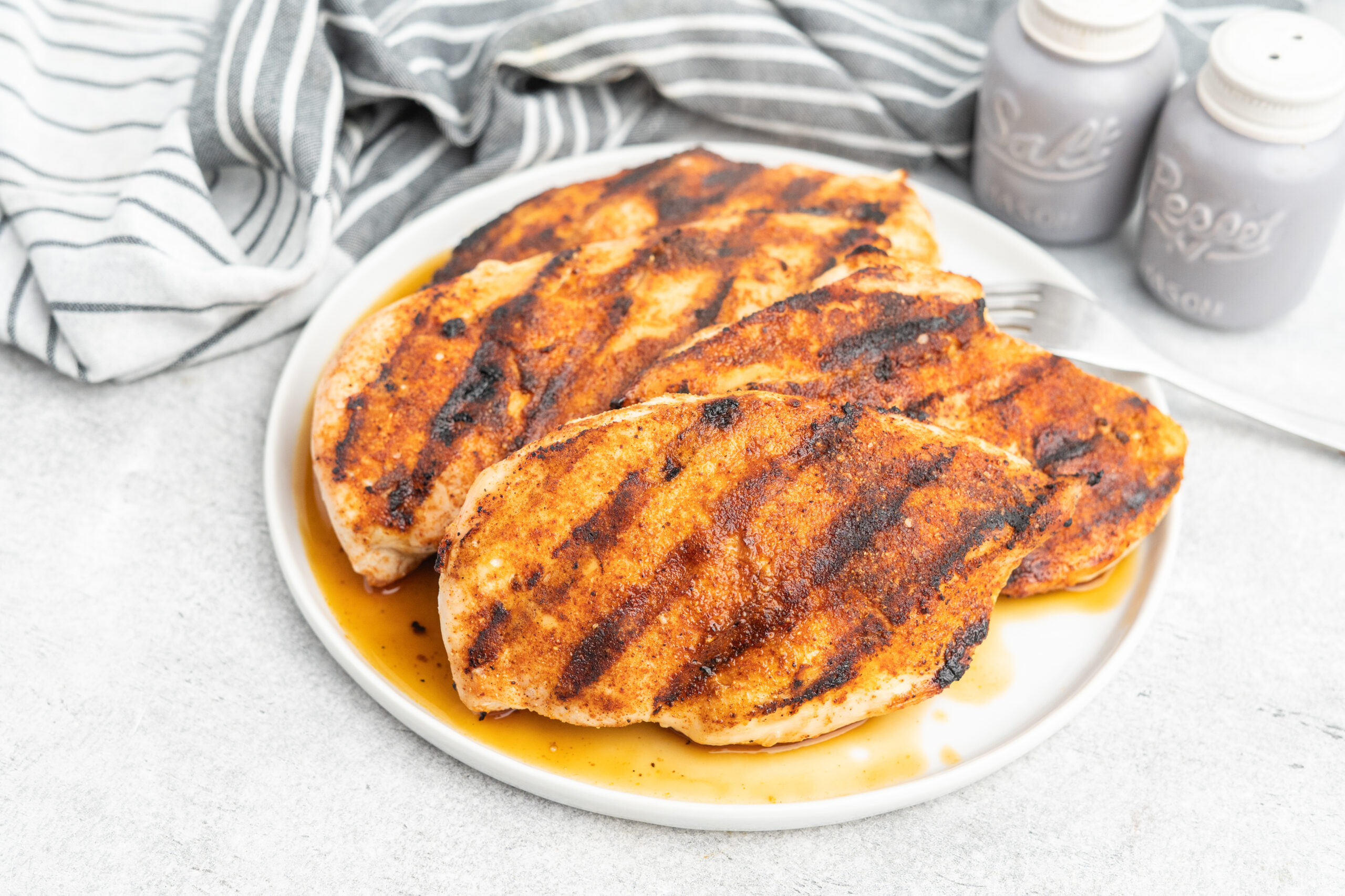 Four seasoned grilled chicken breasts on a plate.