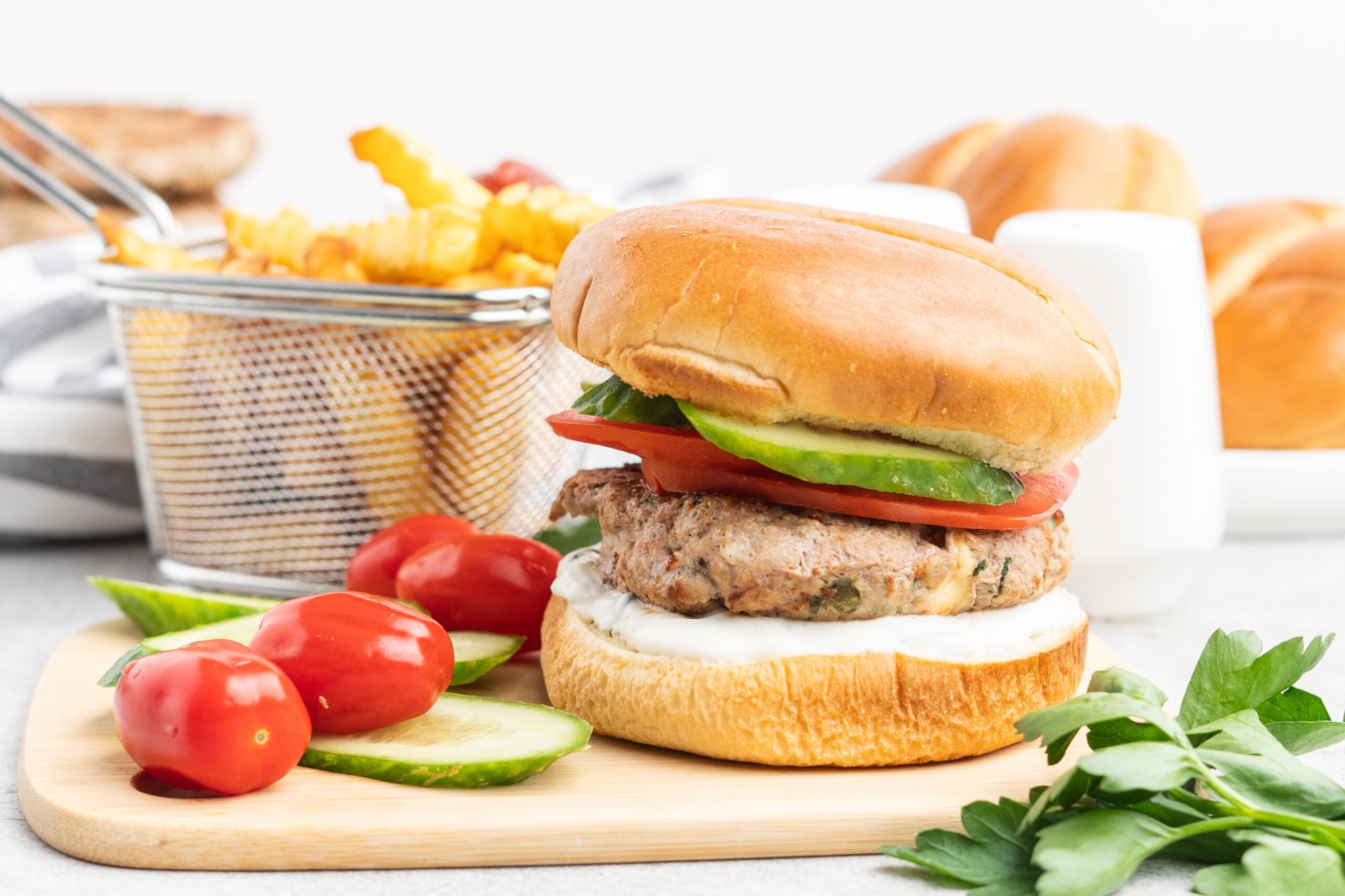 Turkey burger with cucumber and tomato on a brioche bun with a side of french fries.