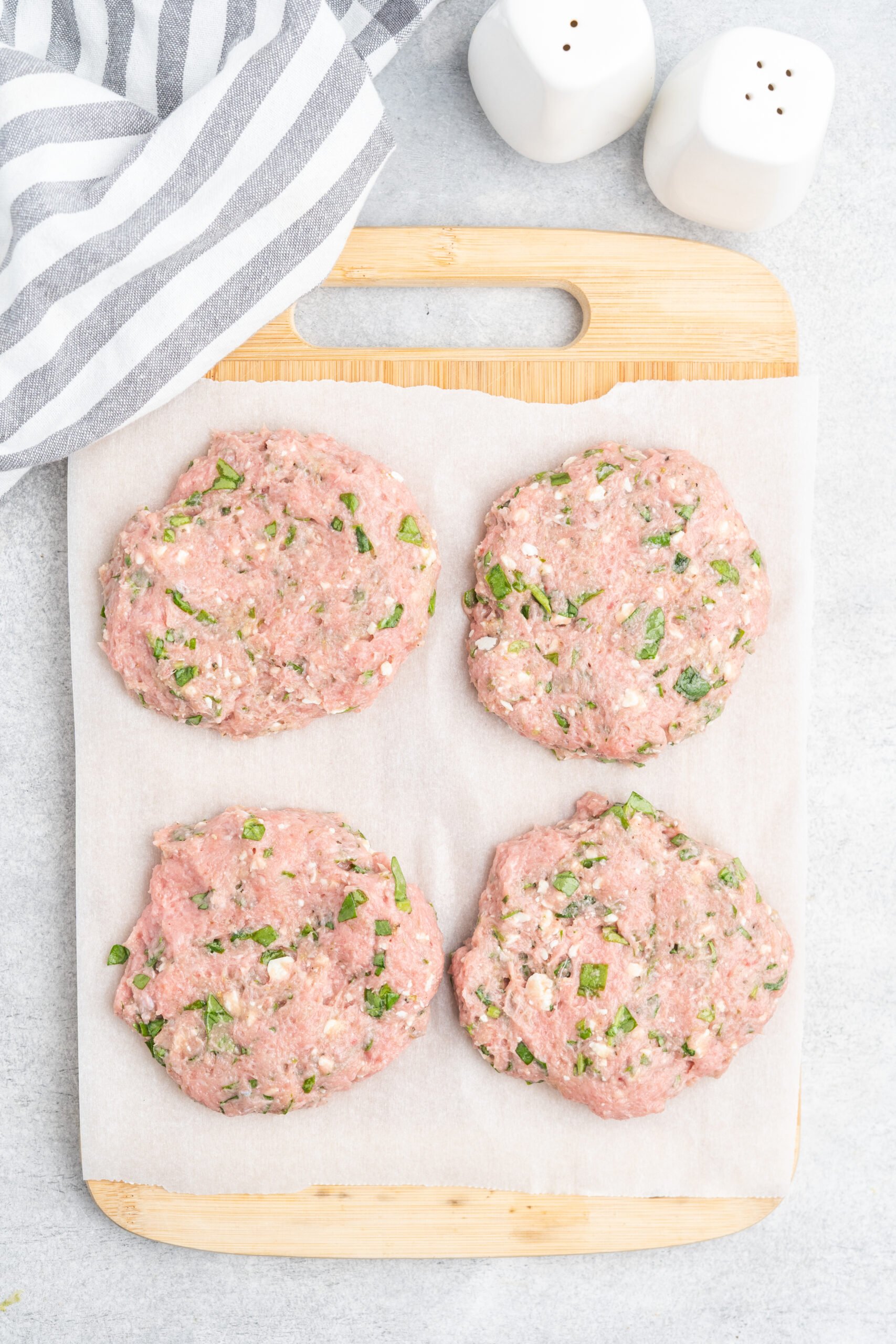 Four raw turkey burger patties on a cutting board lined with parchment paper.