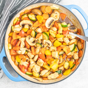 A cast iron skillet with diced vegetables and chicken in sauce.