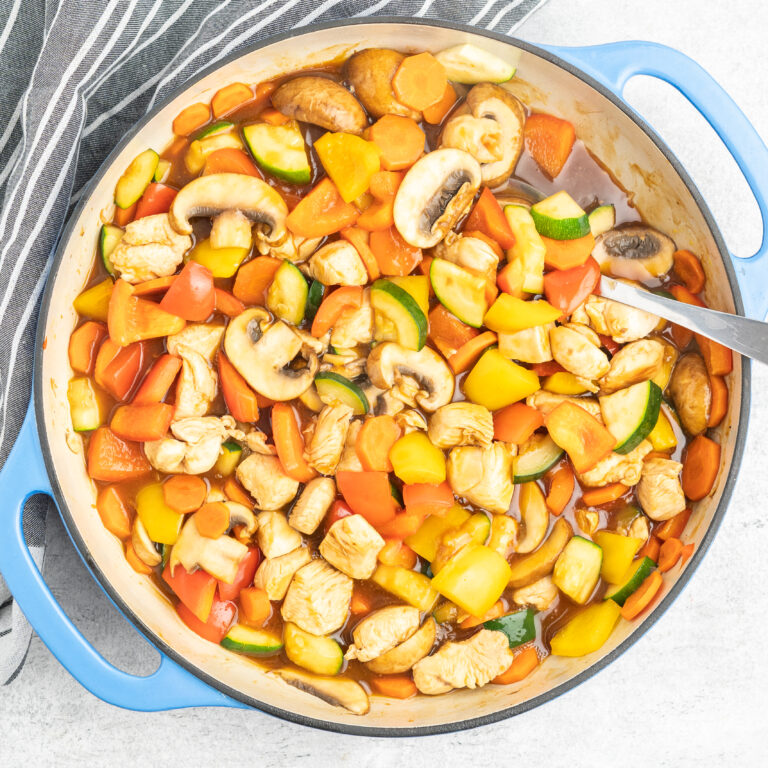 A cast iron skillet with diced vegetables and chicken in sauce.