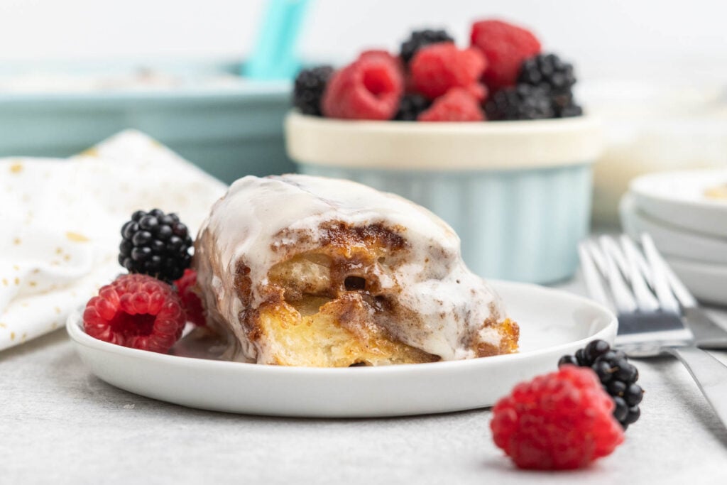 Cinnamon roll with cream cheese frosting on a small plate with fresh berries.