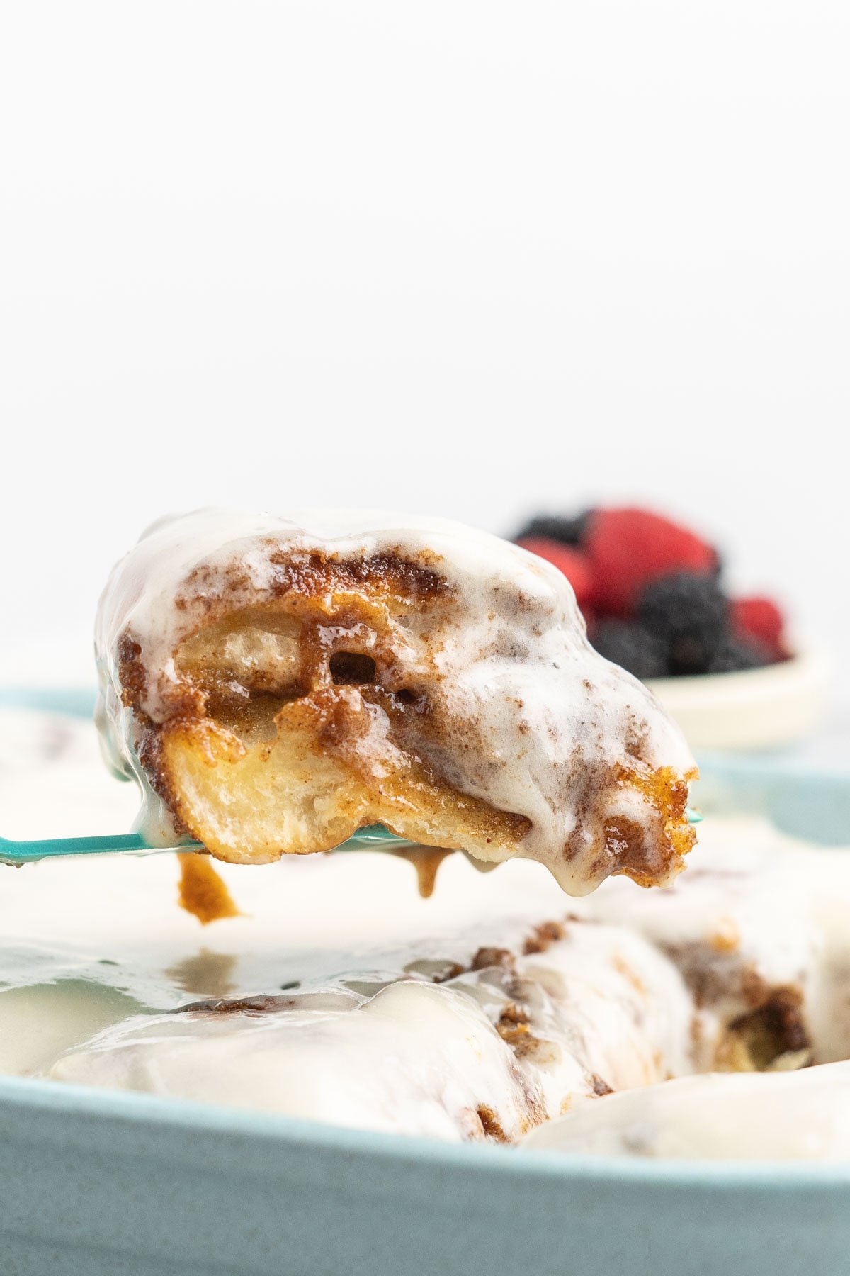 Cinnamon roll with cream cheese frosting being lifted from a pan.