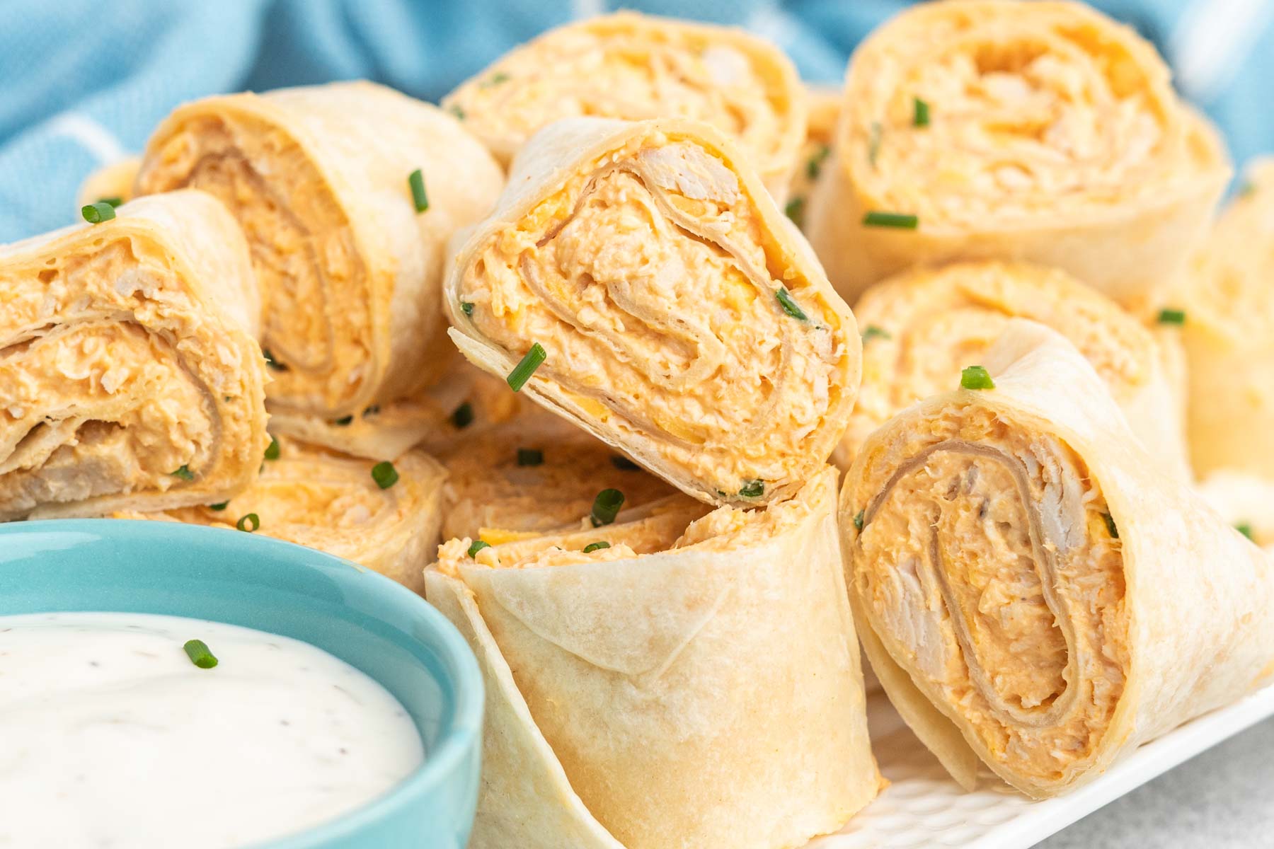 Buffalo chicken rollups in tortillas on a plate with ranch dip.