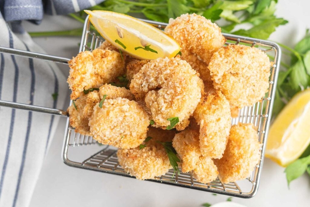 Breaded shrimp in a basket with lemon wedges.